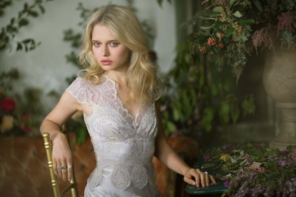 Claire Pettibone wedding dress on blonde model with tossed hair. Sitting in chair looking intense.